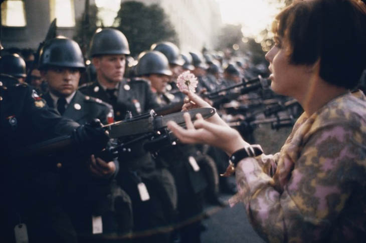 17 year old Jan Rose Kasmir offers a flower to soldiers during the Pentagon anti-war protest in 1967.