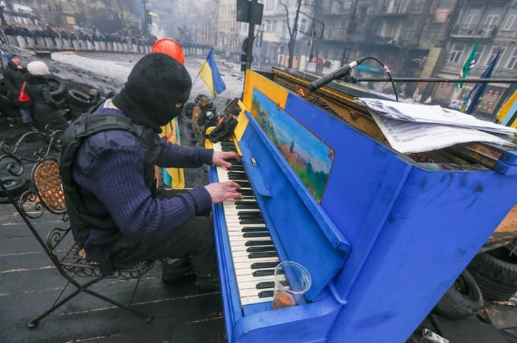 Protester plays piano over the sounds of chaos, with riot police in the backdrop.