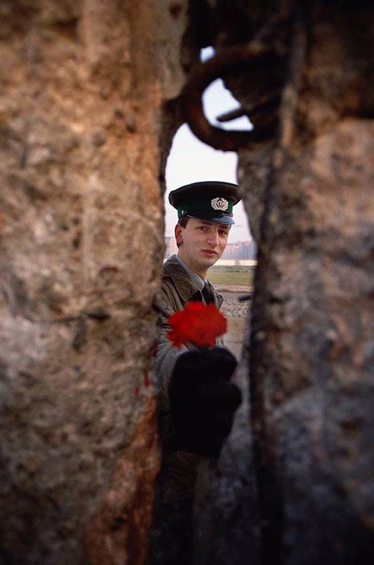1989 - East German soldier passing a flower through the Berlin Wall before it was torn down.